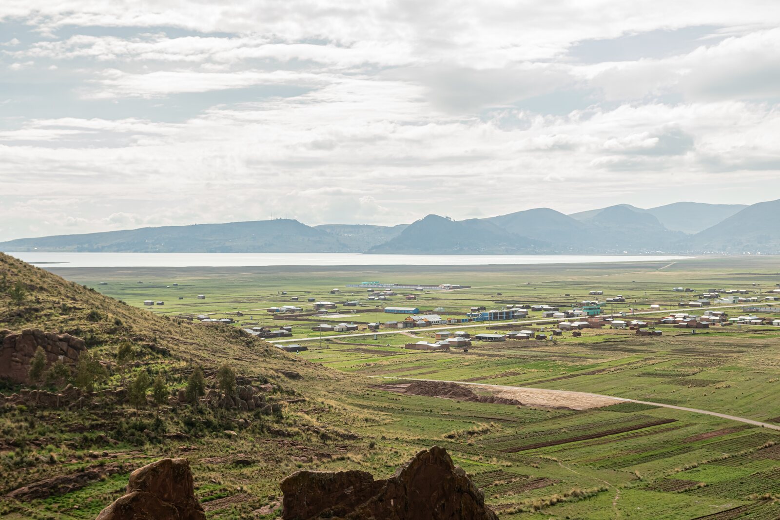 Vista amplia de campos, viviendas, lago y montañas desde el entorno de Aramu Muru, en Ilave.